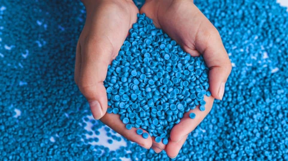 Two hands holding extruded blue plastic pellers indicative of the plastic extrusion plastic